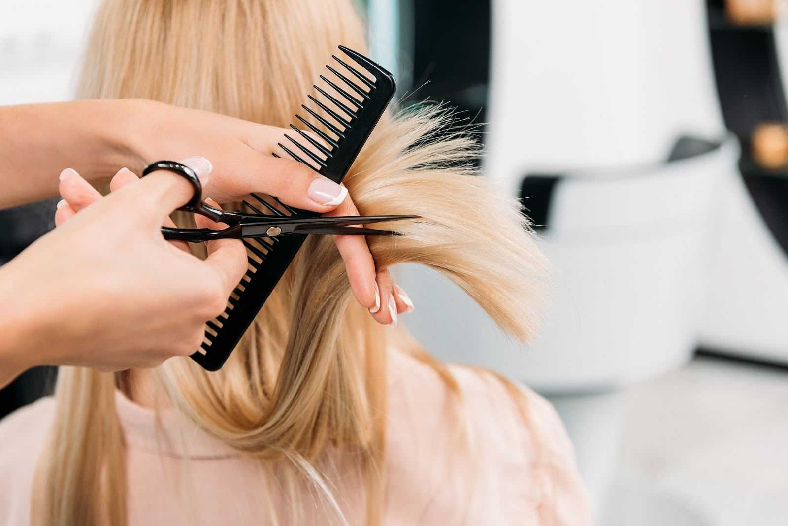 Hairdresser cutting blonde hair with scissors and comb in a salon.